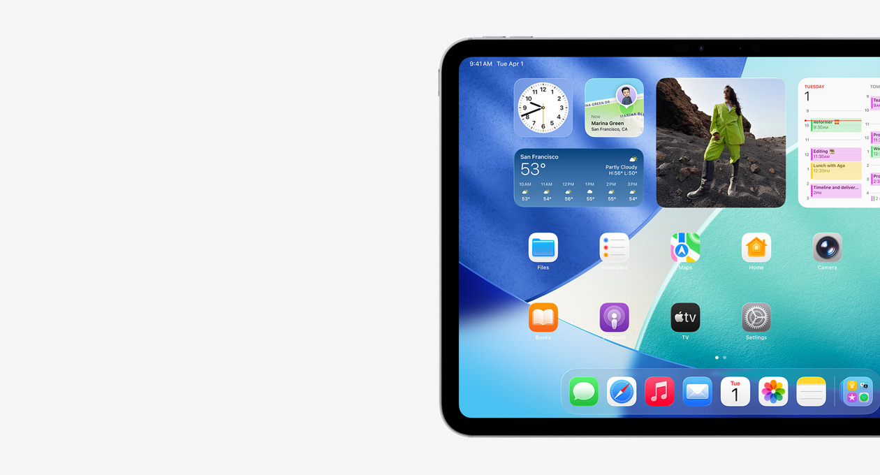 Un iPad, orientation paysage, côté gauche de l’écran uniquement, l’écran d'accueil avec des widgets superposés, notamment une horloge translucide à effet Liquid Glass, l’app Localiser et le widget Météo, deux rangées d'apps plus petites et le Dock