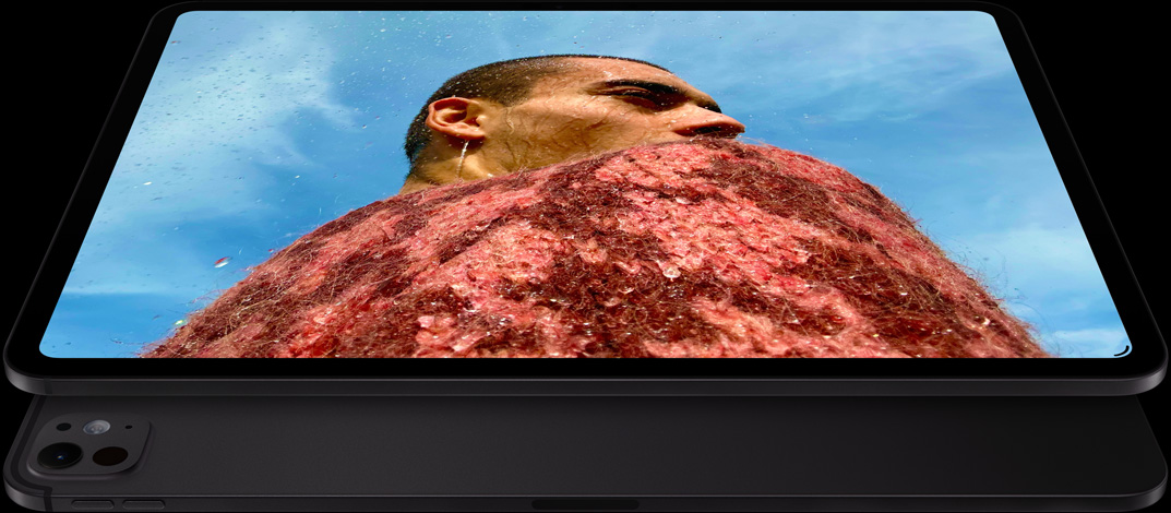 جهاز iPad&nbsp;Pro، الجزء الخارجي الجانبي الأمامي، الوضع الأفقي، لون أسود فلكي، زوايا مدورة، إطار شاشة أسود، شاشة تعرض صورة لرجل يرتدي سترة حمراء تحت سماء زرقاء، وتحته جهاز iPad&nbsp;Pro آخر، الجزء الخارجي الخلفي، الوضع الأفقي، لون أسود فلكي، نظام كاميرات Pro، زر رفع مستوى الصوت، زر خفض مستوى الصوت